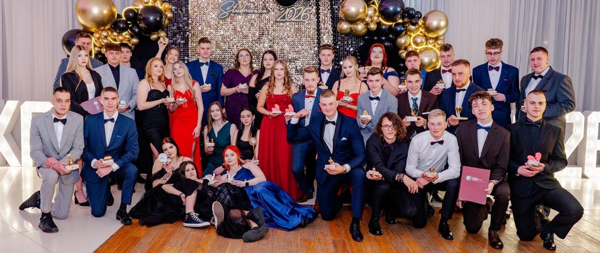 Grupa uczniów pozuje do zdjęcia trzymając w rękach statuetki