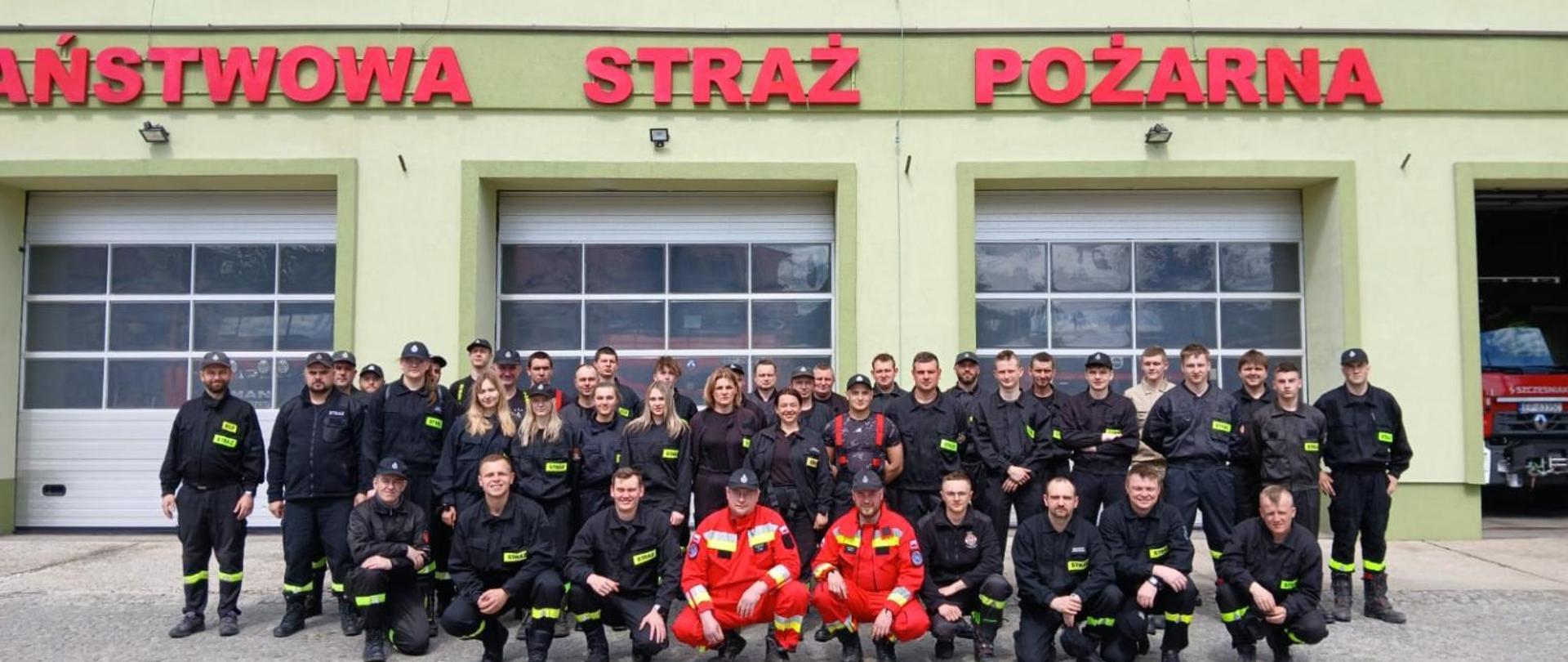 Na tle budynku KM PSP w Piotrkowie Trybunalskim zdjęcie grupowe uczestników szkolenia strażaków ratowników OSP. Strażacy w umundurowaniu koszarowym.