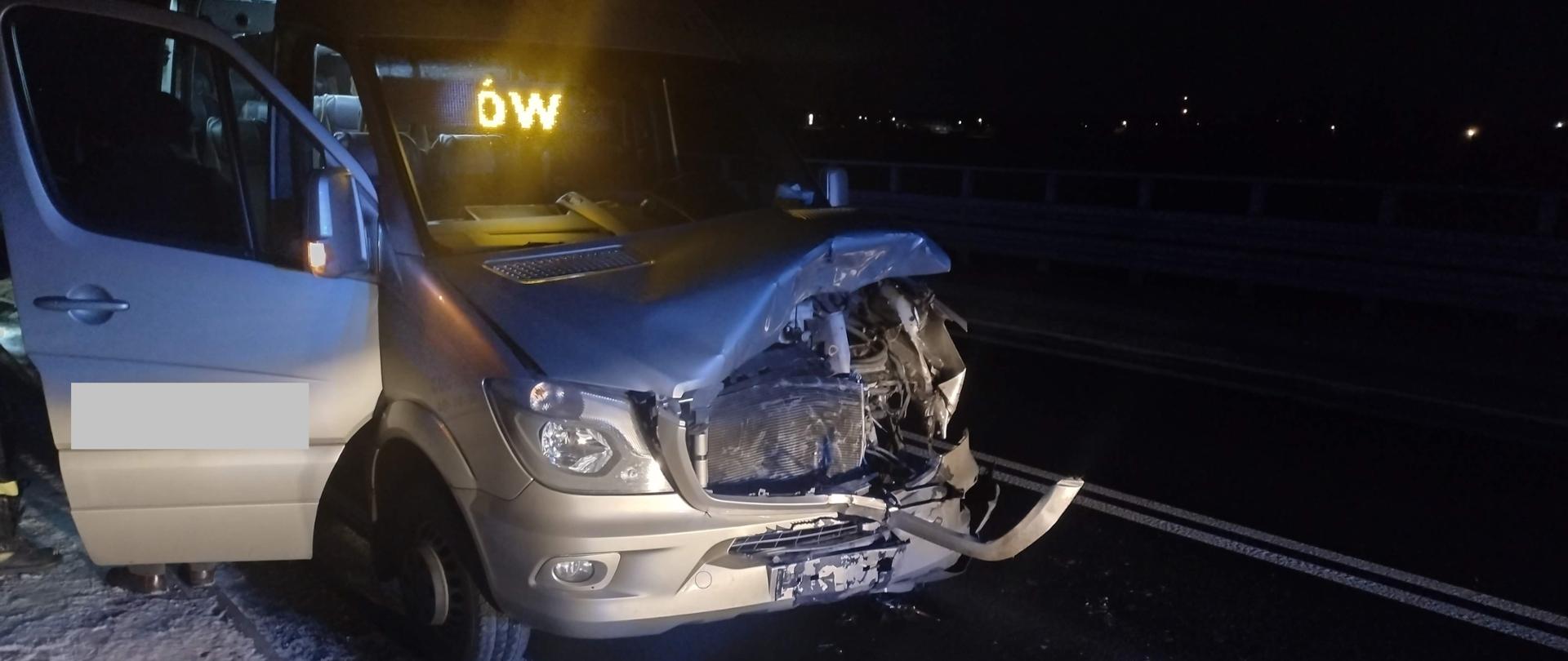 W porze nocnej widać przód rozbitego busa, który stoi na jednym pasie drogi. Kolizja busa z jeleniem.