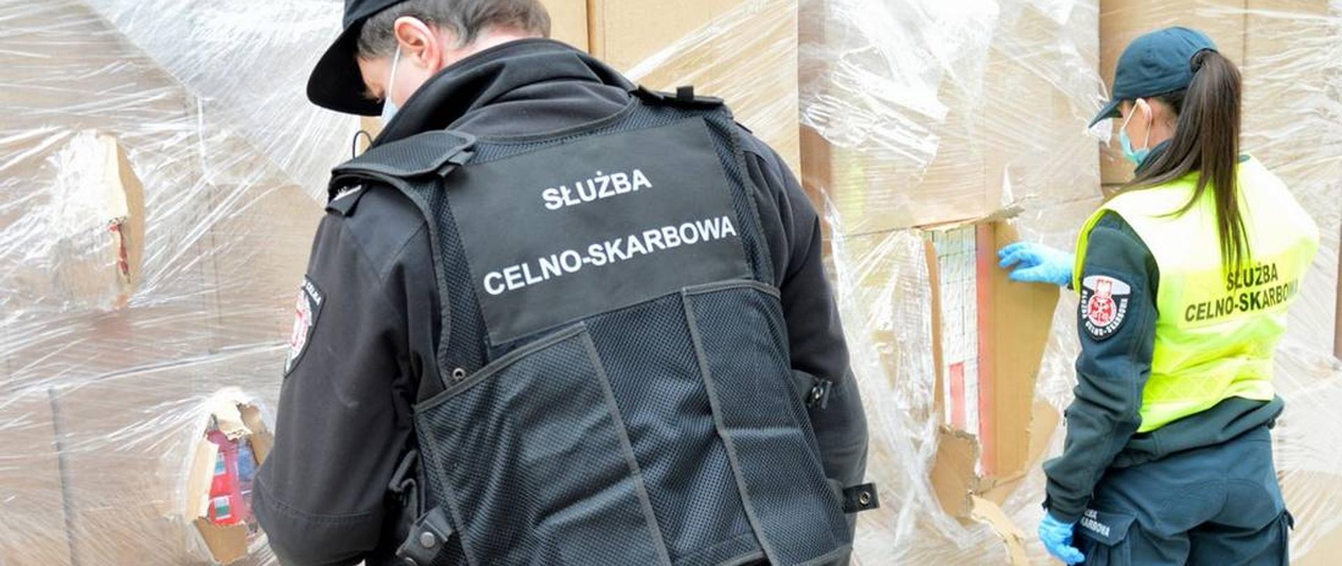 Funkcjonariusz i funkcjonariuszka Służby Celno-Skarbowej podczas sprawdzania zafoliowanych kartonów z papierosami.