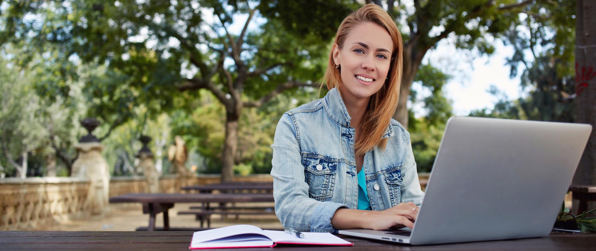Uśmiechnięta dziewczyna siedzi z laptopem w parku