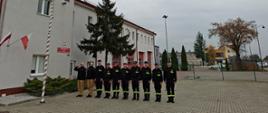 Strażacy stoją na placu jednostki i przy maszcie z flagą odśpiewali hymn państwowy. 