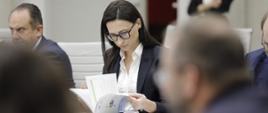 Obrady Rady Wykonawczej ds. wdrażania Krajowej Polityki Miejskiej 2030, przy stole obrad siedzi wiceminister klimatu i środowiska Małgorzata Golińska i przegląda broszurę
