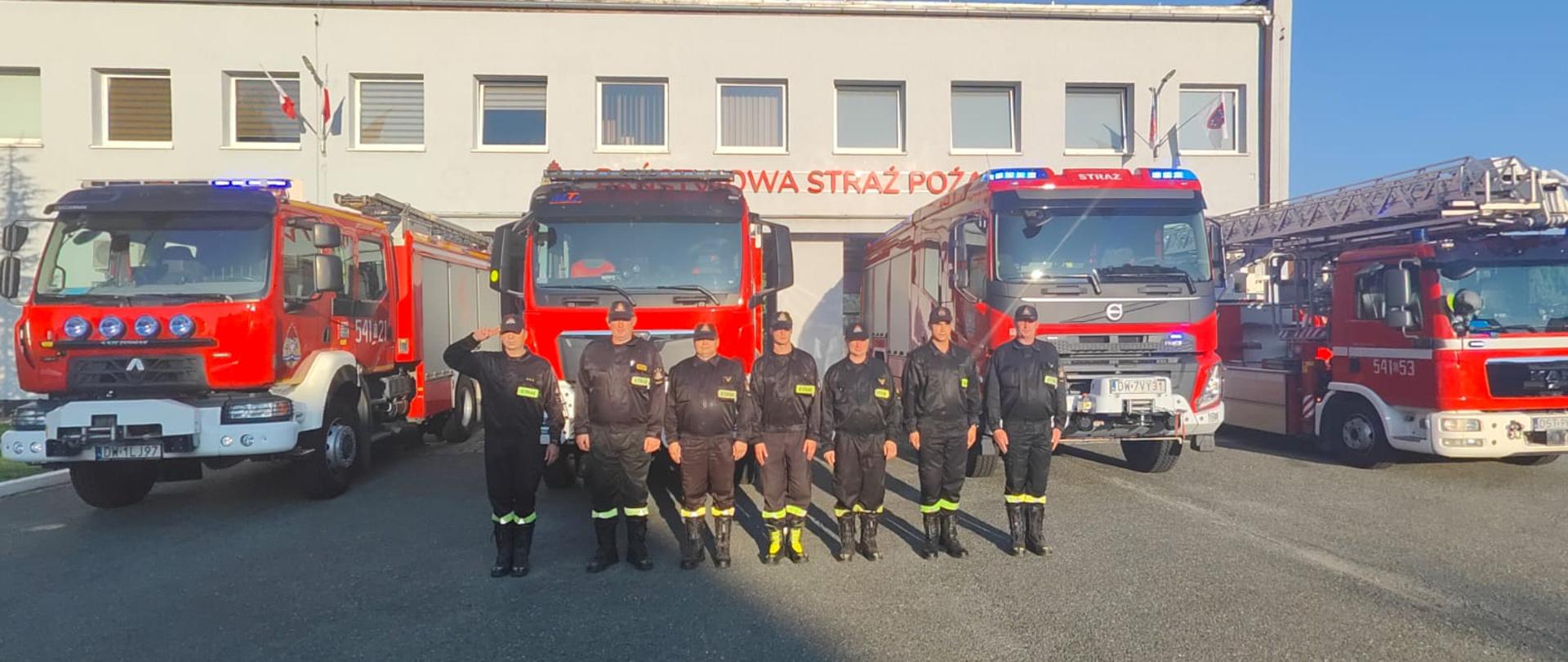 Strażacy oddali hołd na tle pojazdów pożarniczych