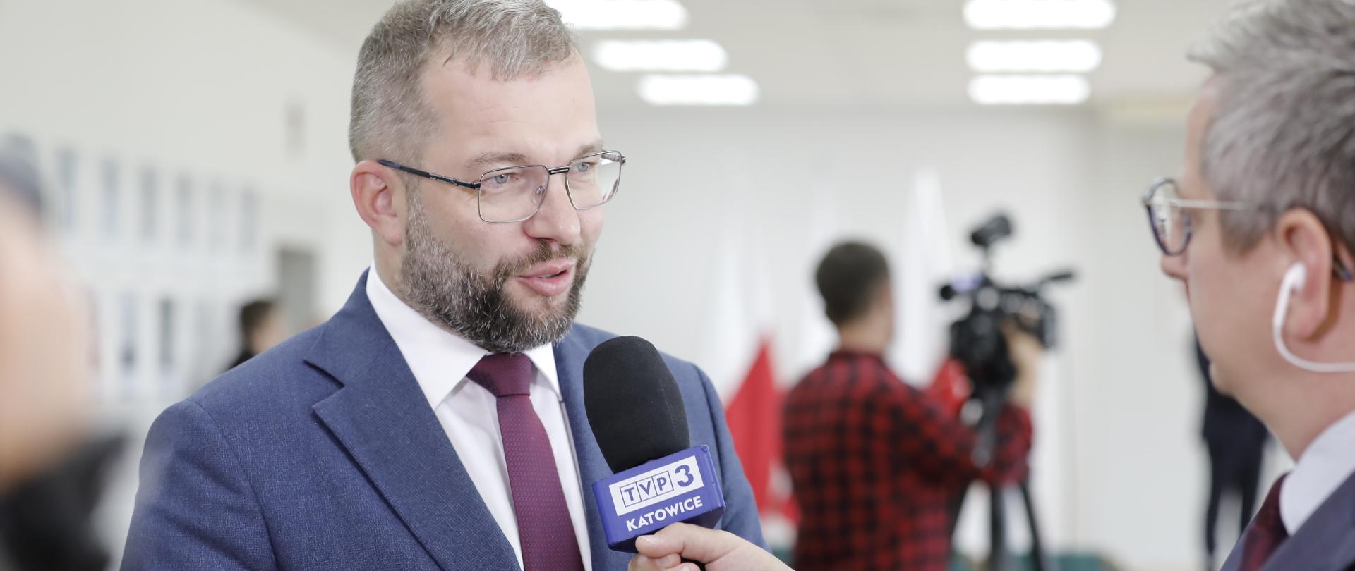 Minister funduszy i polityki regionalnej Grzegorz Puda stoi przy mikrofonie TVP Katowice i udziela wywiadu dziennikarzowi