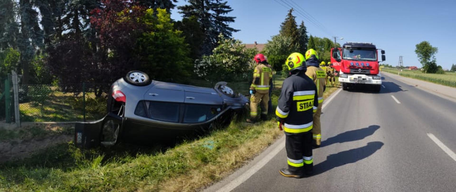 Na zdjęciu dwa samochody strażackie oraz auto w rowie znajdujące sią na dachu