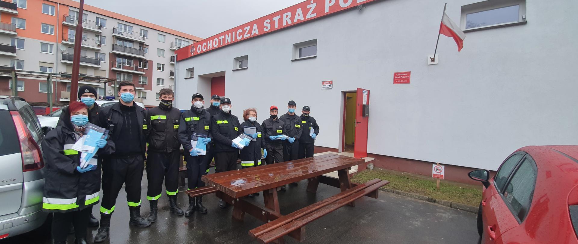 Na zdjęciu druhowie OSP ubrani w umundurowanie koszarowe, stojący w szeregu. W rękach trzymają ulotki.