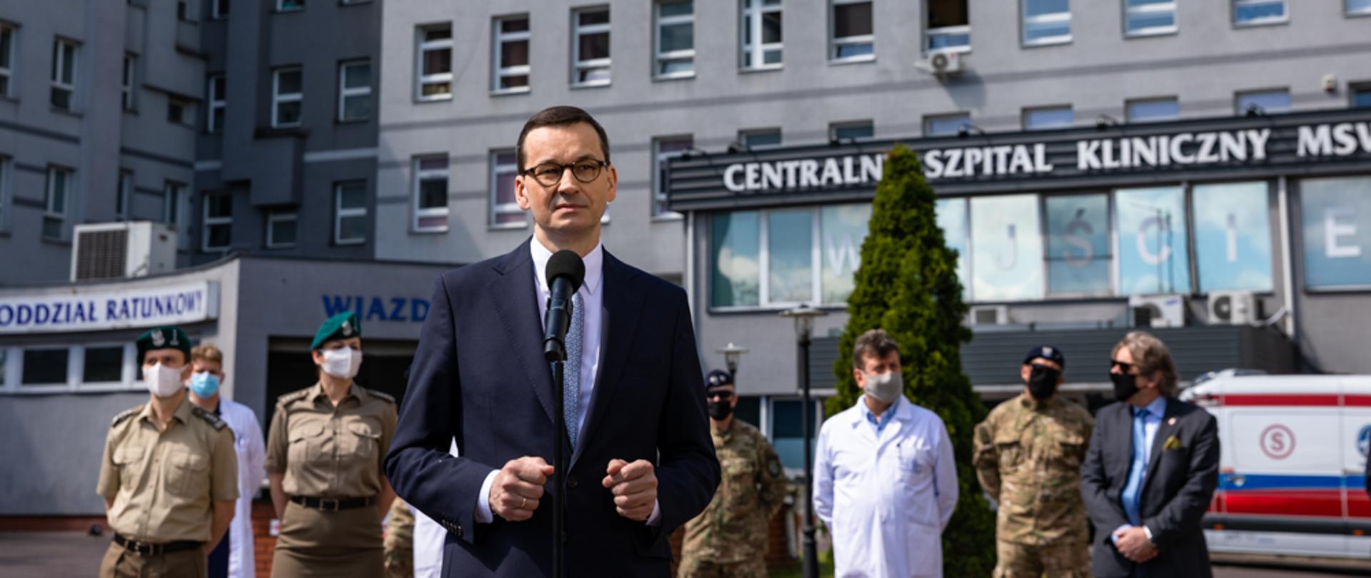 Premier Mateusz Morawiecki stoi podczas konferencji prasowej.