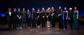 zdjęcie przedstawia wszystkich uczestników koncertu we wspólnym zdjęciu z instrumentami na scenie sali koncertowej