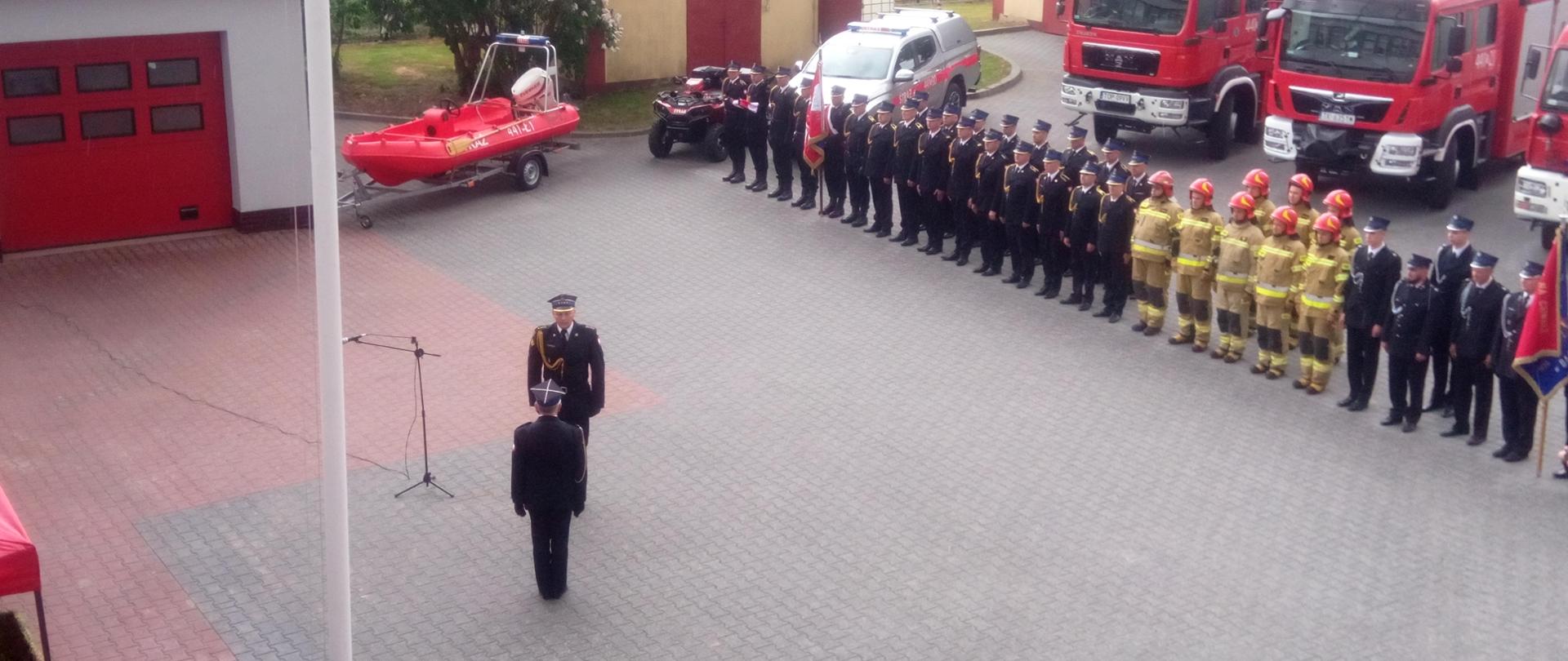 Zdjęcie przedstawia dowódcę uroczystości, który składa meldunek zastępcy Świętokrzyskiego Komendanta Wojewódzkiego w Kielcach. W tle widać strażaków stojących w dwuszeregu 