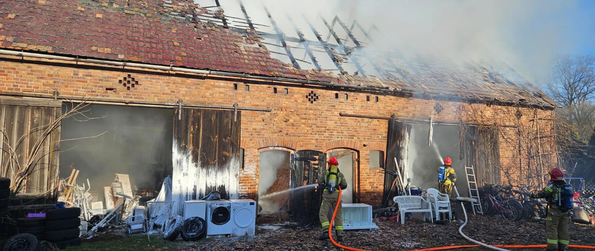 Strażacy prowadzą działania gaśnicze budynku gospodarczego.