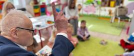 mężczyzna w garniturze, wicewojewoda, podnosi palec do góry, patrzy na dzieci, czyta książkę 