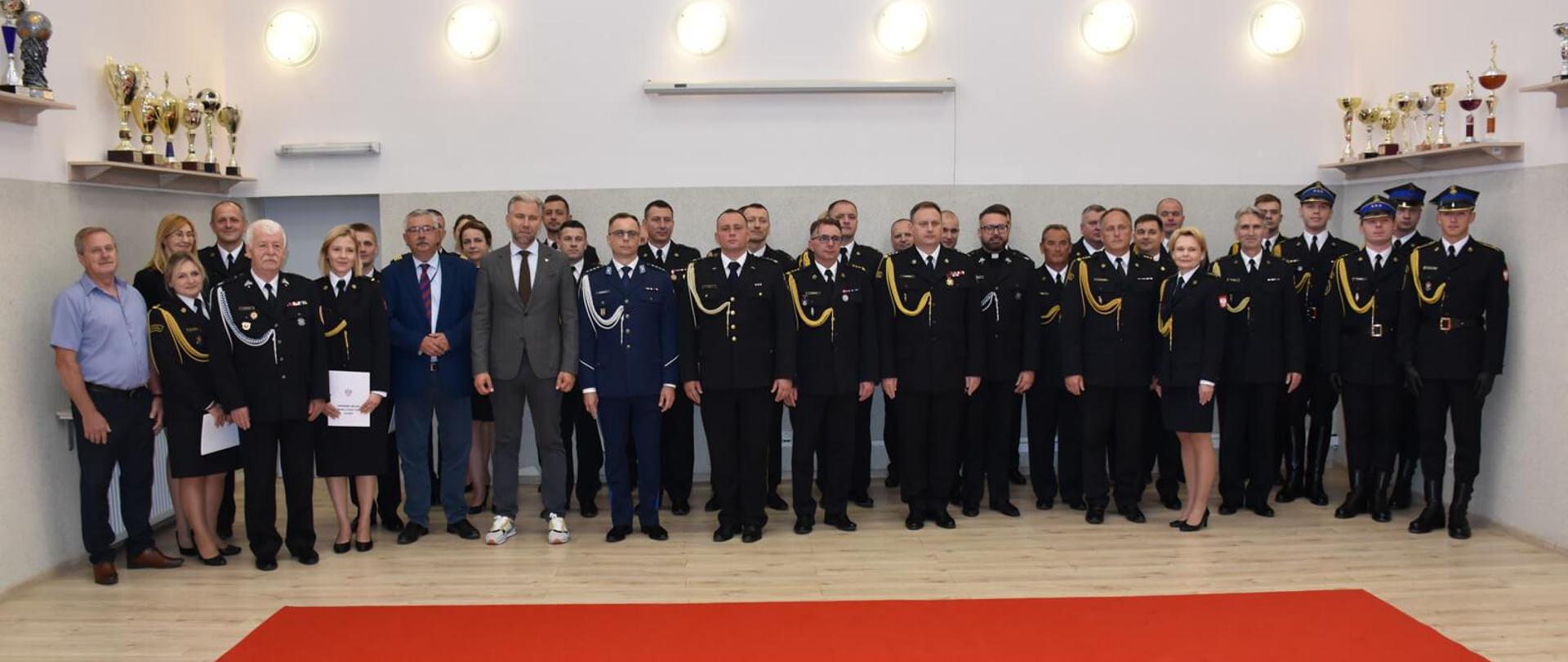 strażacy i inni uczestnicy uroczości pozują do zdjęcia w sali konferencyjnej