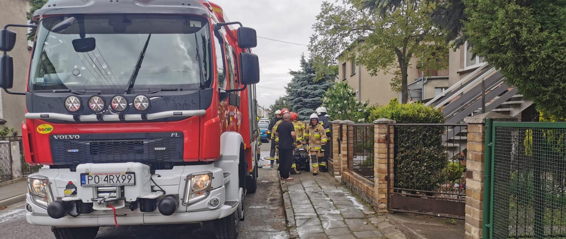 Wóz strażacki stoi na ulicy obok strażacy.