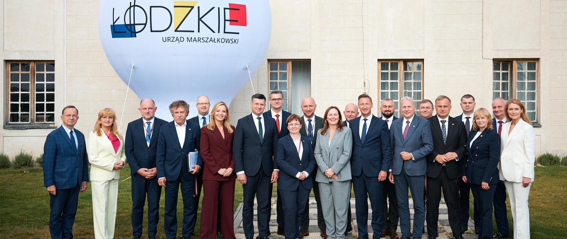 Kilkanaście osób stoi obok siebie na trawniku.