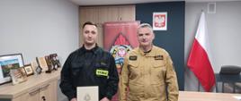 Komendant Powiatowy Państwowej Straży Pożarnej w Człuchowie st. bryg. Radosław Batruch stoi w gabinecie i wręcza akt mianowania na stanowisko ratownika w służbie stałej st. str. Dawidowi Synoradzkiemu.