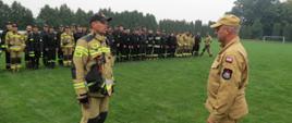 Zdjęcie przedstawia st. kpt. Roberta Czarneckiego Zastępcę Dowódcy JRG w Brodnicy składającego meldunek o zakończeniu ćwiczeń st. bryg. Robertowi Wiśniewskiemu Zastępcy Kujawsko-Pomorskiego Komendanta Wojewódzkiego PSP. W oddali strażacy uczestniczący w ćwiczeniach.