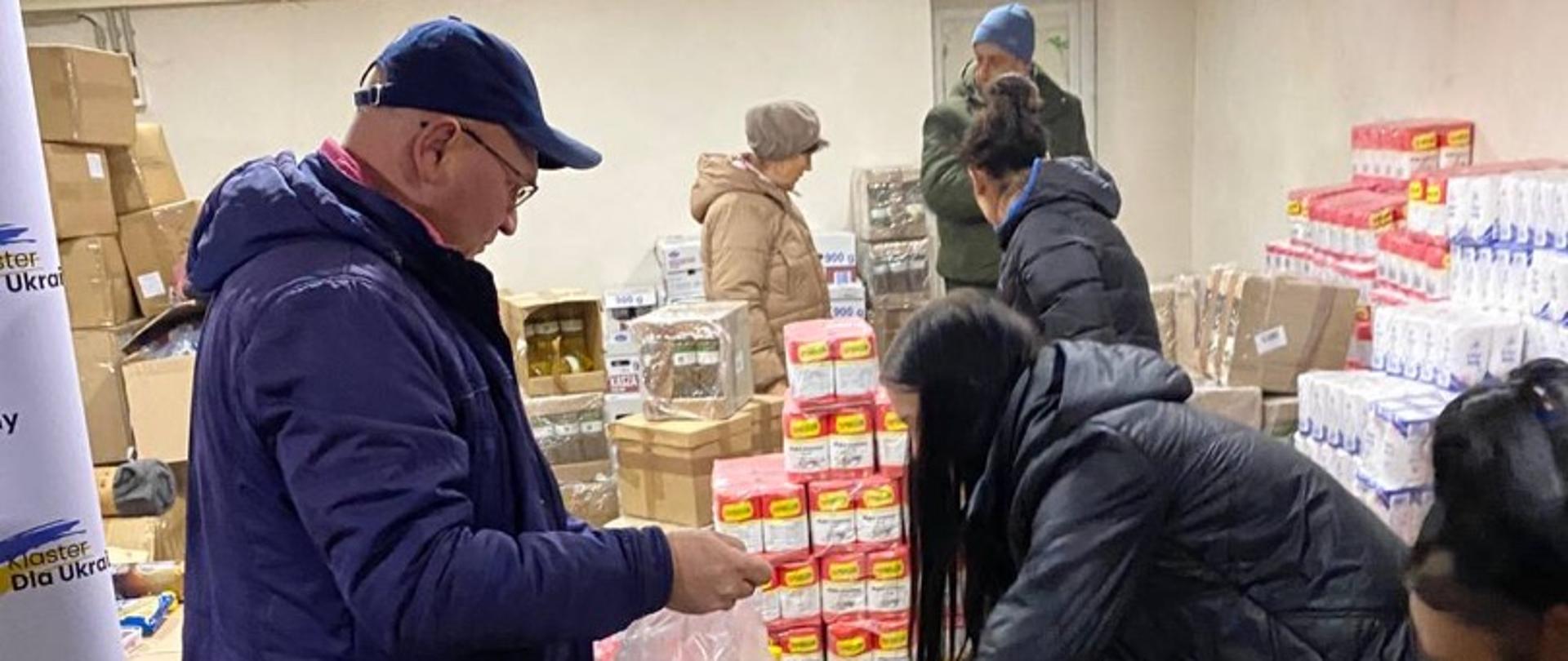 W magazynie grupa osób pakuje produkty żywnościowe do plastikowych siatek