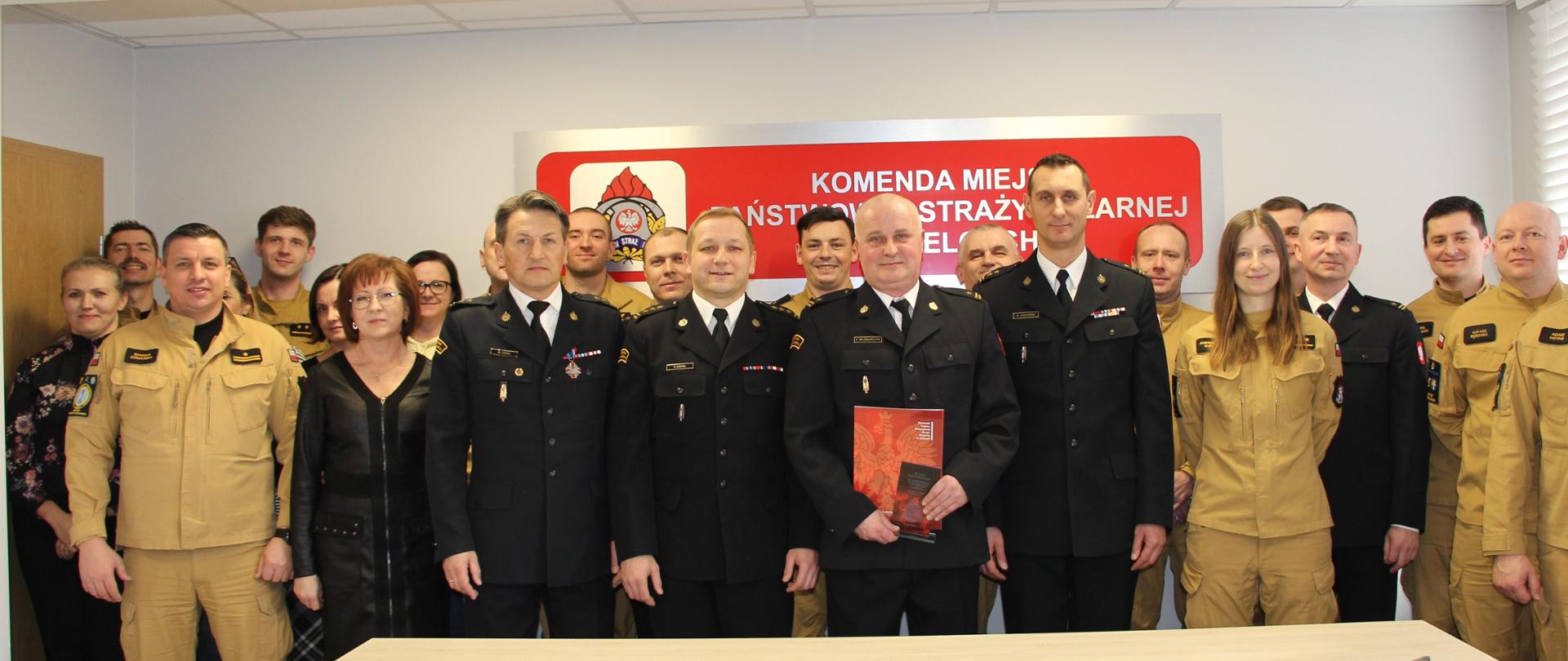 Zdjęcie przedstawia współpracowników zebranych na uroczystości pożegnania odchodzącego emeryta w sali konferencyjnej Komendy Miejskiej PSP w Kielcach