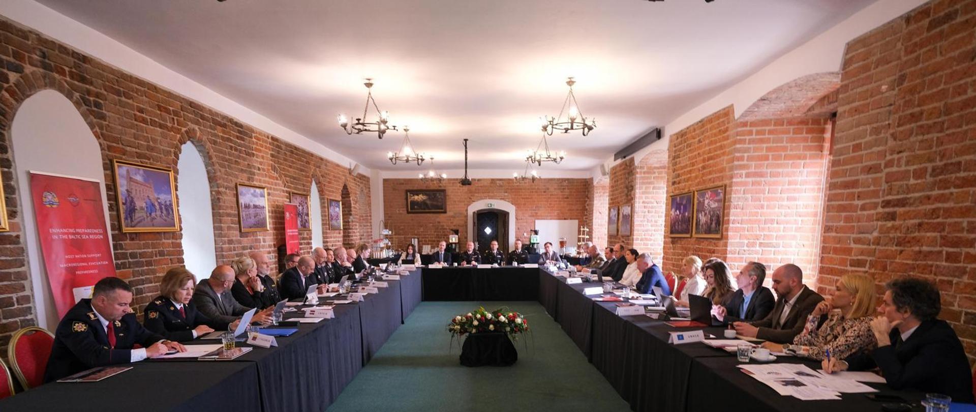 Uczestnicy 24. Posiedzenia Dyrektorów Generalnych Ochrony Ludności Rady Państw Morza Bałtyckiego siedzą przy stołach ustawionych w sali konferencyjnej.