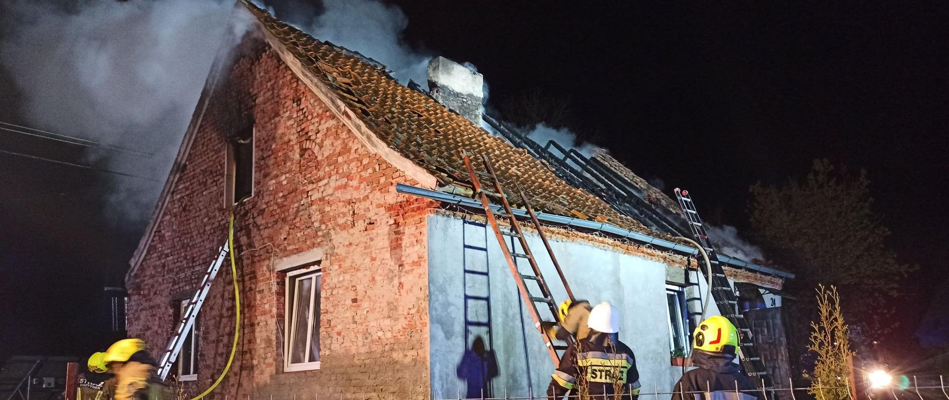 Na zdjęciu widać spalony dach budynku oraz strażaków w trakcie prowadzonych działań gaśniczych