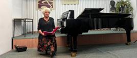 Pani Jolanta Reszelska siedzi obok fortepianu prowadząc wykład