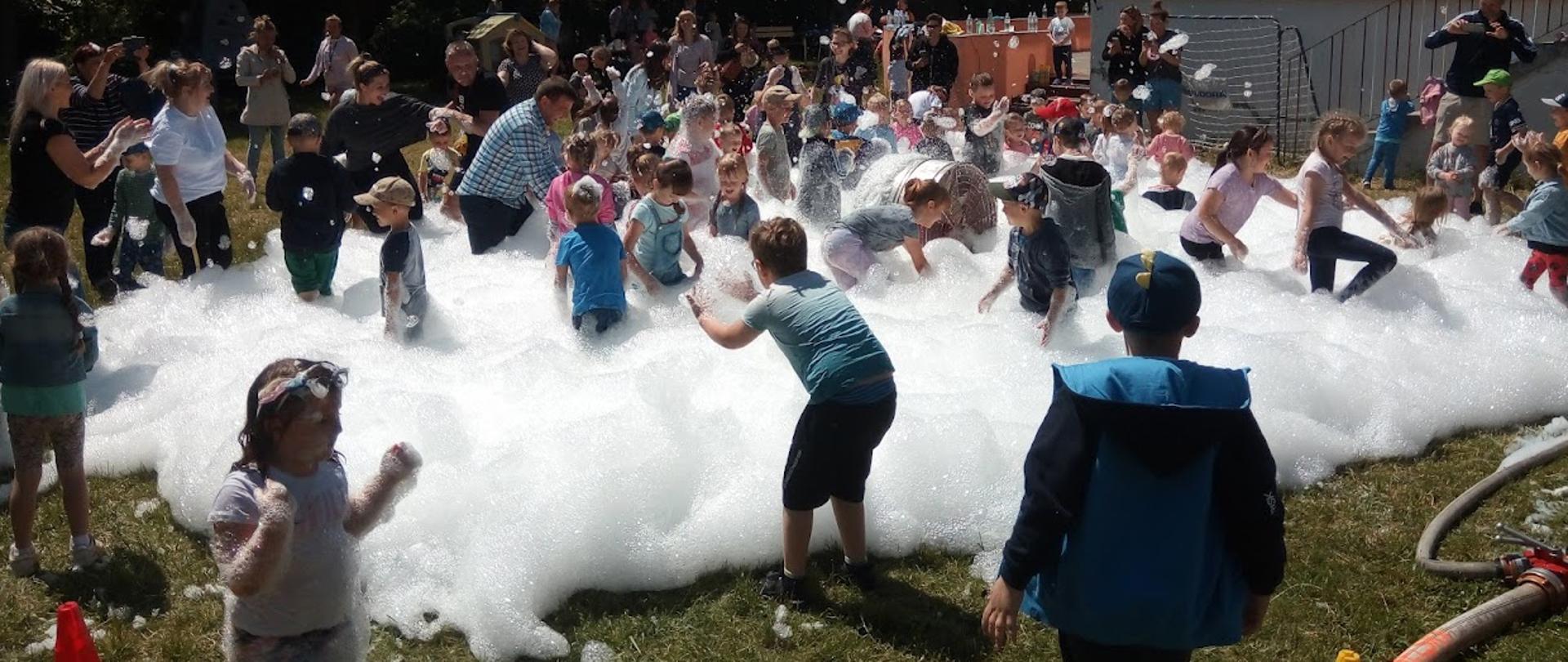 Zdjęcie przedstawia dzieci i opiekunów podczas zabawy w pianie na swieżym powietrzu 
