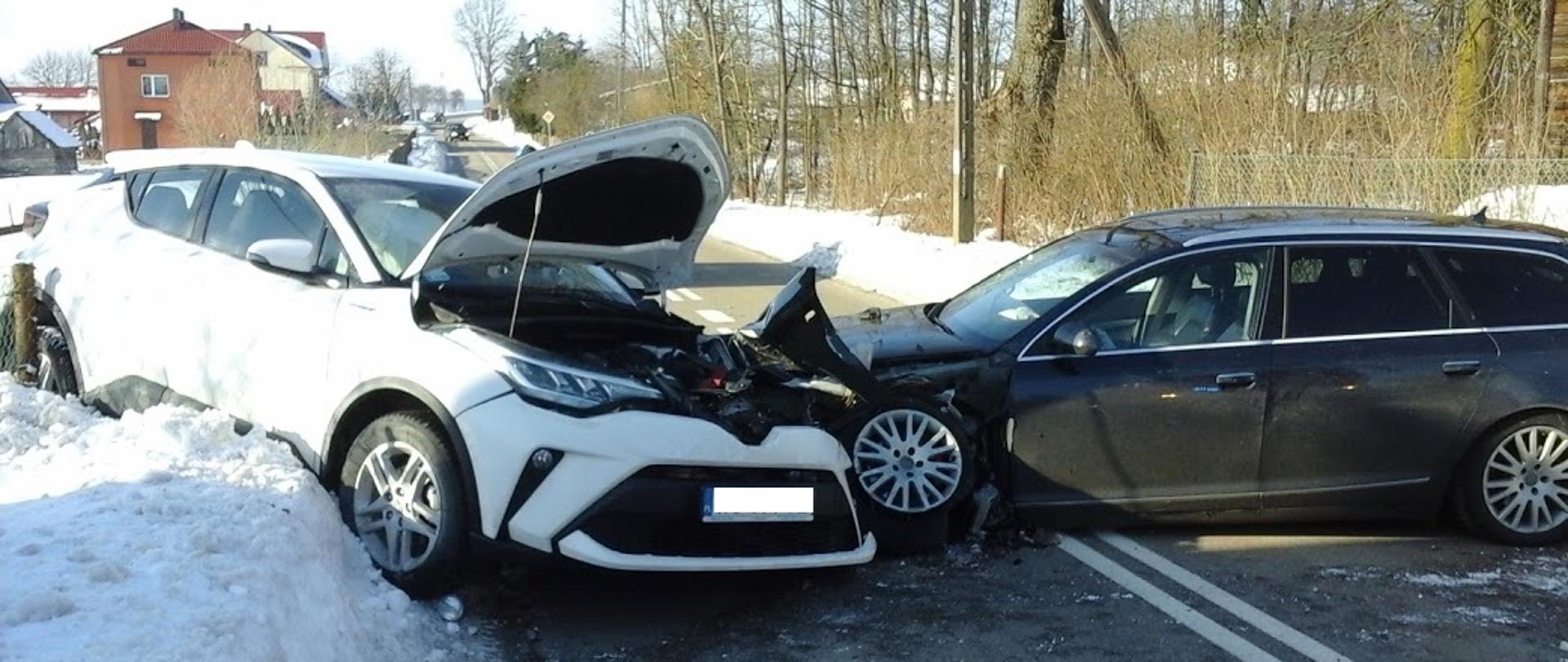 Na zdjęciu widać dwa rozbite auta osobowe. Białe auto Toyota znajduje się na skarpie śniegu