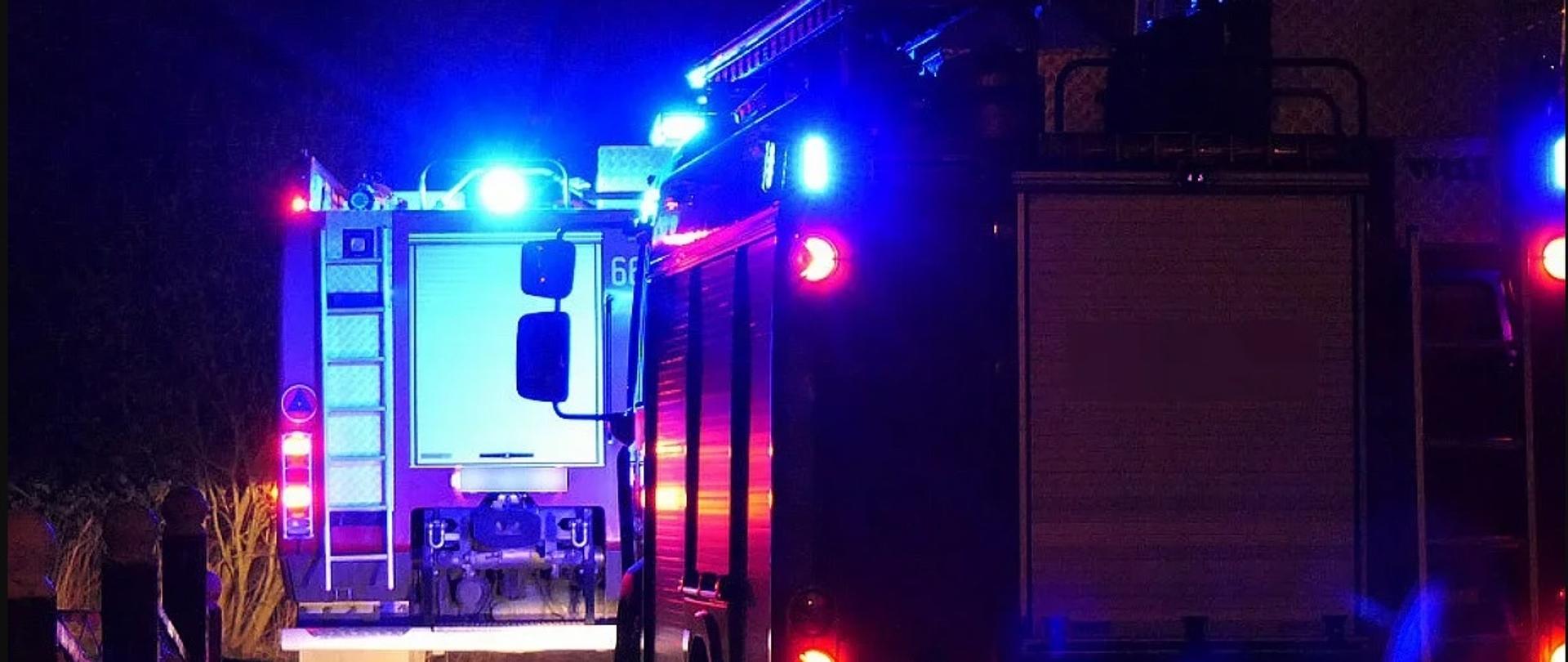 Zdjęcie poglądowe przedstawiające pojazdy straży pożarnej na włączonych światłach błyskowych koloru niebieskiego.