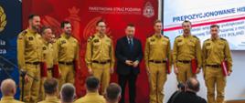 Grupa strażaków w mundurach na scenie wraz z mezczyna z garniturze.