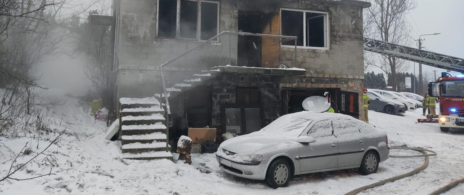 Zdjęcie przedstawia budynek jednorodzinny gdzie wybuchł pożar. Po prawej stronie widać samochód pożarniczy.