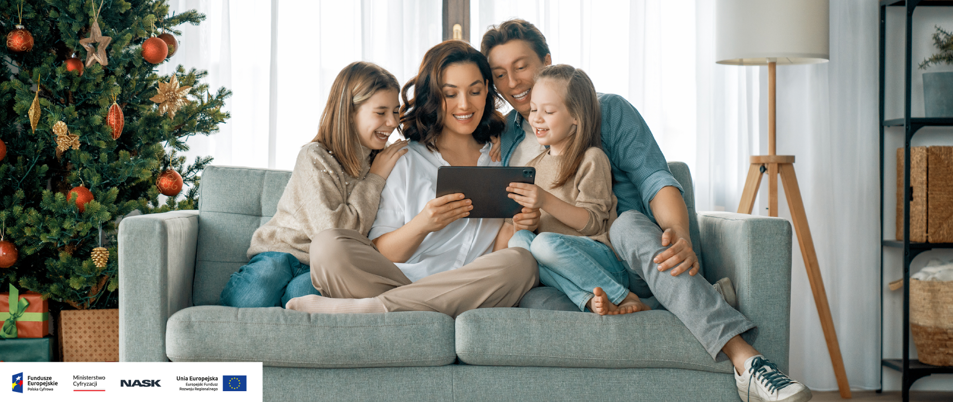 Grafika ze zdjęciem przedstawiającym rodzinę (rodzice i dwoje dzieci) siedzącą na kanapie przy choince. Wszyscy patrzą w tablet. W lewym dolnym rogu logotypy: Fundusze Europejskie, Ministerstwo Cyfryzacji, NASK, Unia Europejska.