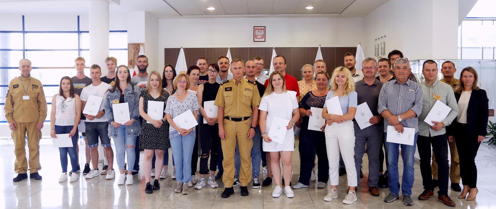 Grupowe zdjęcie uczestników szkolenia (27 osób) w towarzystwie Zastępcy Komendanta Centralnej Szkoły PSP, kobiety oraz dwóch funkcjonariuszy CS PSP