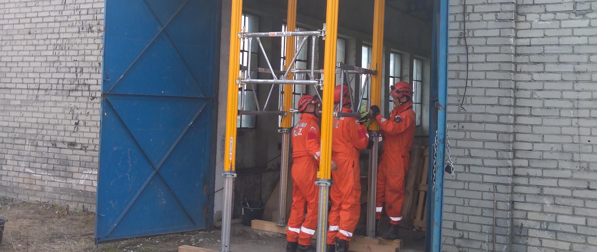 Trzech ratowników SGPR ŁOMŻA podczas stabilizacji wejścia do budynku podporami metalowymi