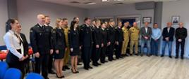 Uczestnicy uroczystości – funkcjonariusze PSP, pracownicy cywilni oraz zaproszeni goście – ustawieni do pamiątkowego zdjęcia. Spotkanie odbyło się w sali Komendy Powiatowej PSP w Wolsztynie.