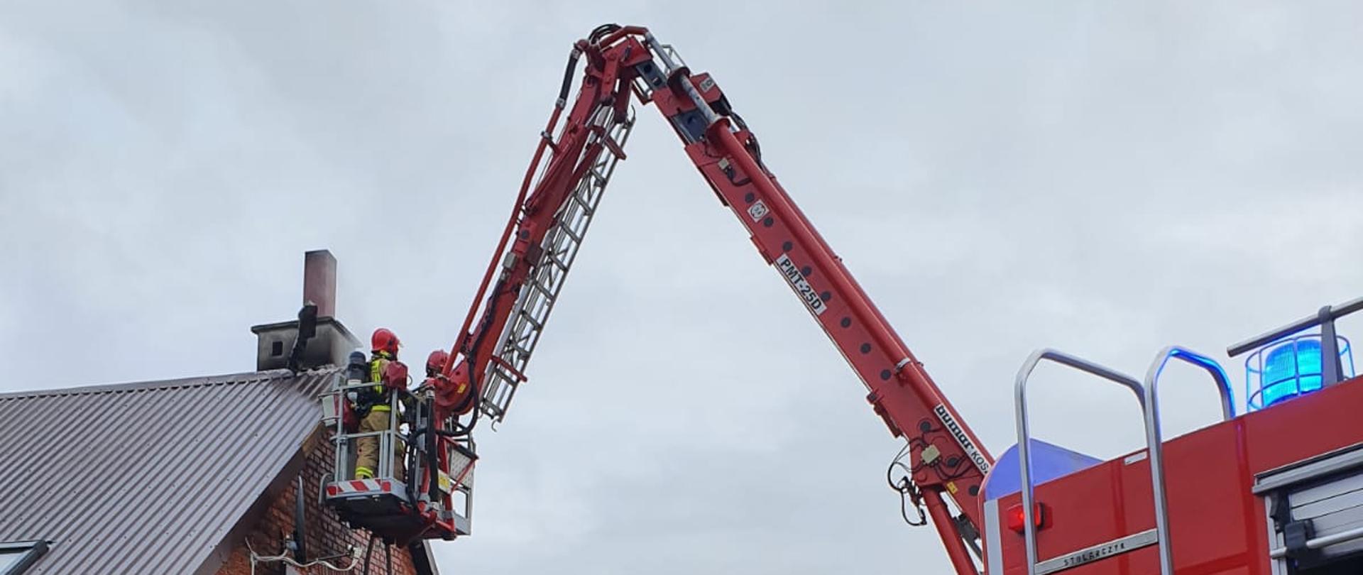 Na zdjęciu widać strażaków pracujących w koszu podnośnika, budynek oraz część wozu strażackiego