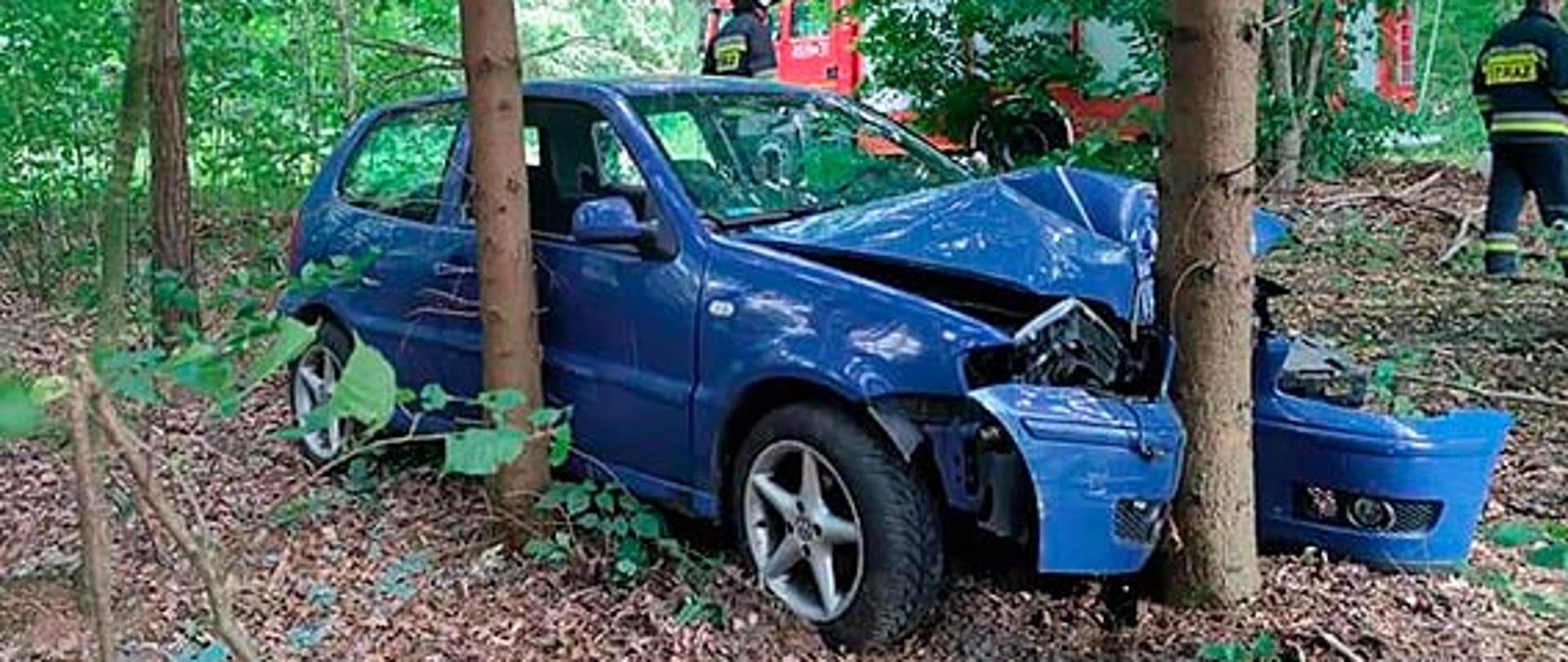 Niebieski pojazd rozbity na drzewie w lesie.