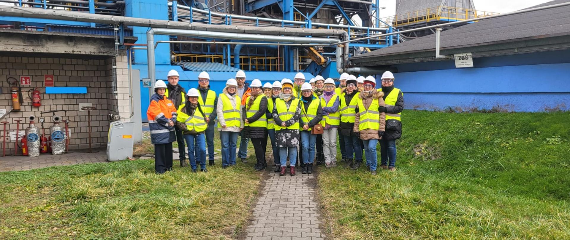 grupa pracowników w żółtych kamizelkach i kaskach przed siedzibą spółki