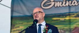 Mężczyzna w eleganckim stroju wygłasza przemówienie z podium na wydarzeniu.