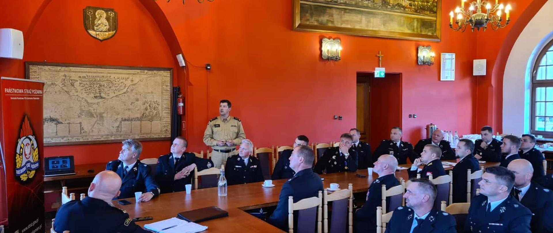 Na zdjęciu widoczny przemawiający st. bryg. Marek Popławski, widoczni druhowie ochotnicy podczas prezentacji na temat ustawy o OSP. Widoczna charakterystyczna sala UM w Kamieniu Pomorskim