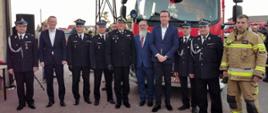 goście w ilości dziesięciu osób stoją przed samochodem strażackim pozując do pamiątkowego zdjęcia
