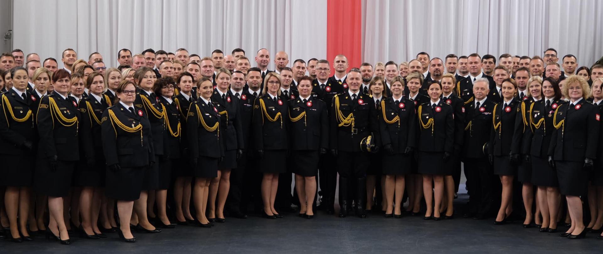 Zdjęcie grupowe prawie 200 funkcjonariuszy. wszyscy w mundurach galowych - w tle flaga biało-czerwona i godło narodowe.
