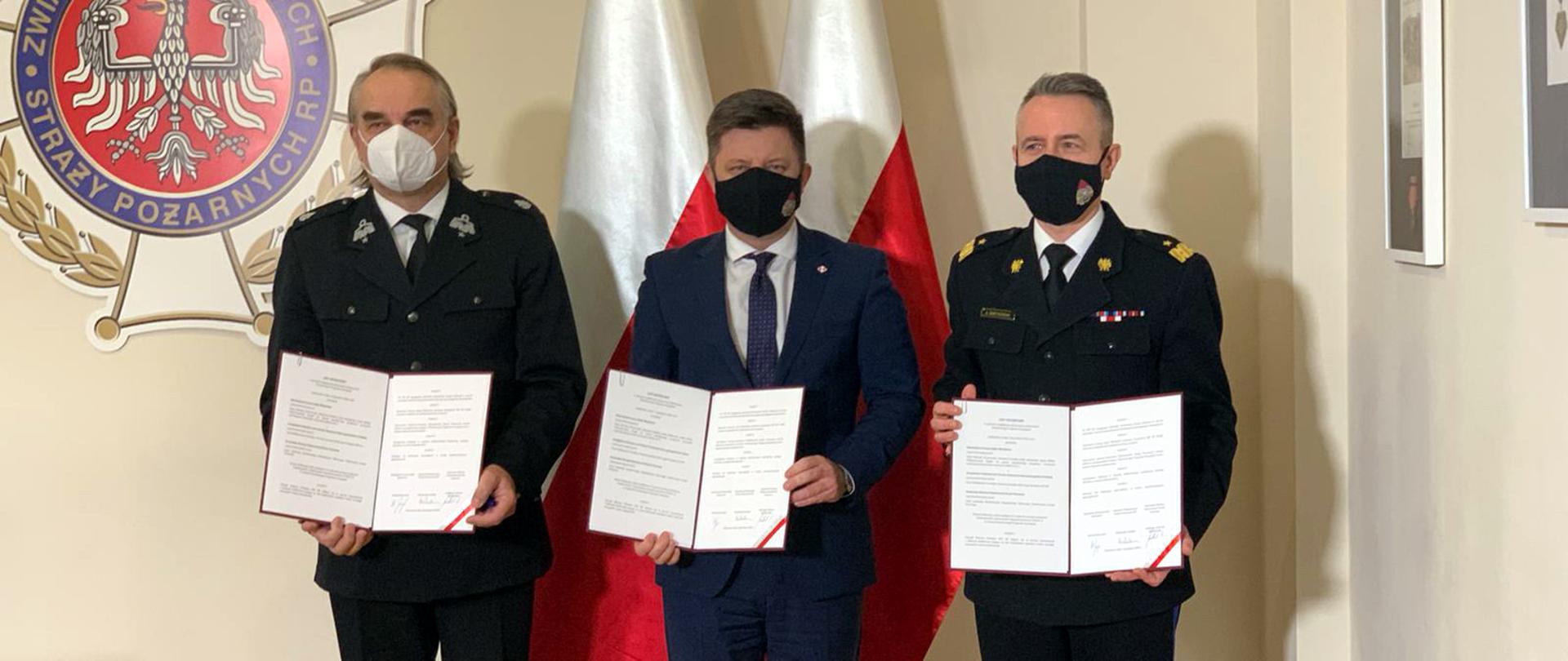 KG Ministrem oraz W.Pawlakiem prezentują treść listu intencyjnego na tle biało-czerwonej flagi 