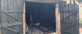Na zdjęciu widać otwarte spalone drzwi do budynku gospodarczego