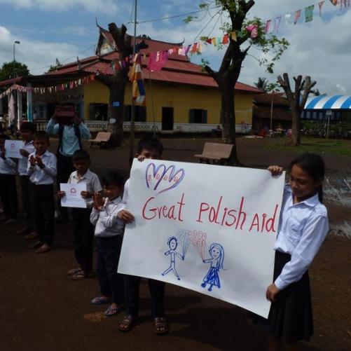 dzieci ubrane w uroczyste stroje galowe trzymają napis Great Polish Aid