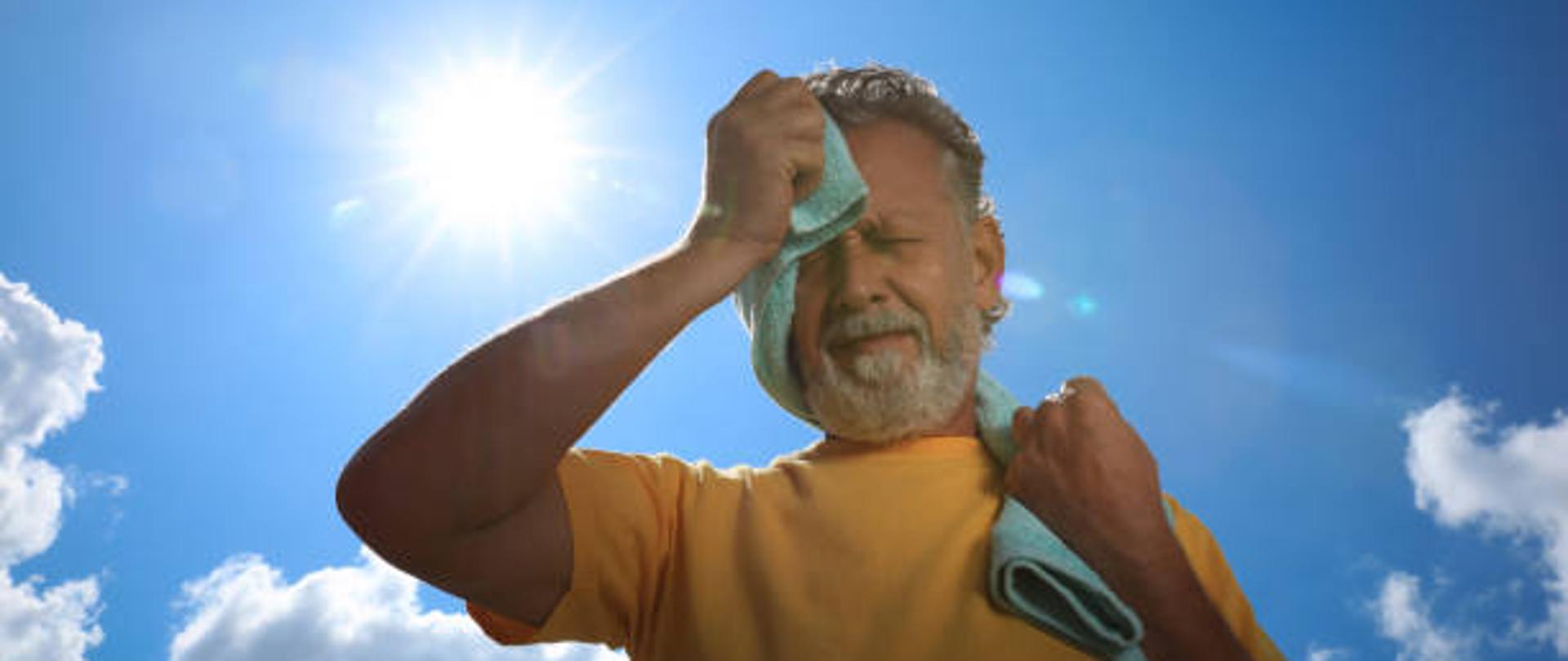 Senior man with towel suffering from heat stroke outdoors, low angle view
