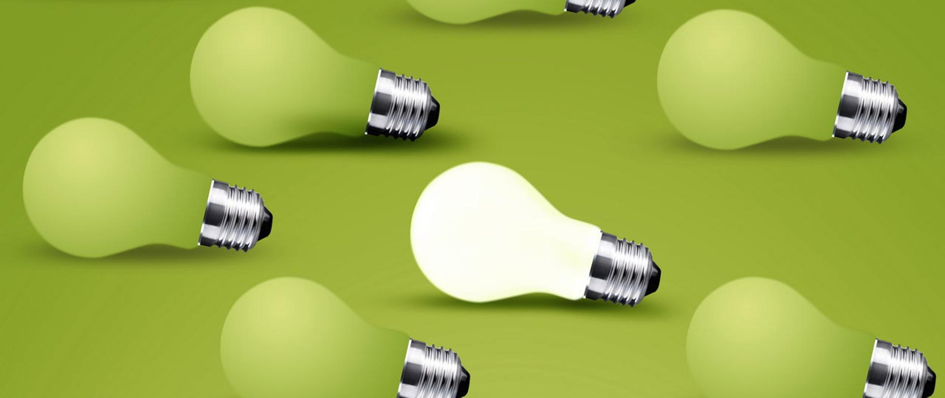 Żarówki na zielonym tle, jedna żarówka świeci.