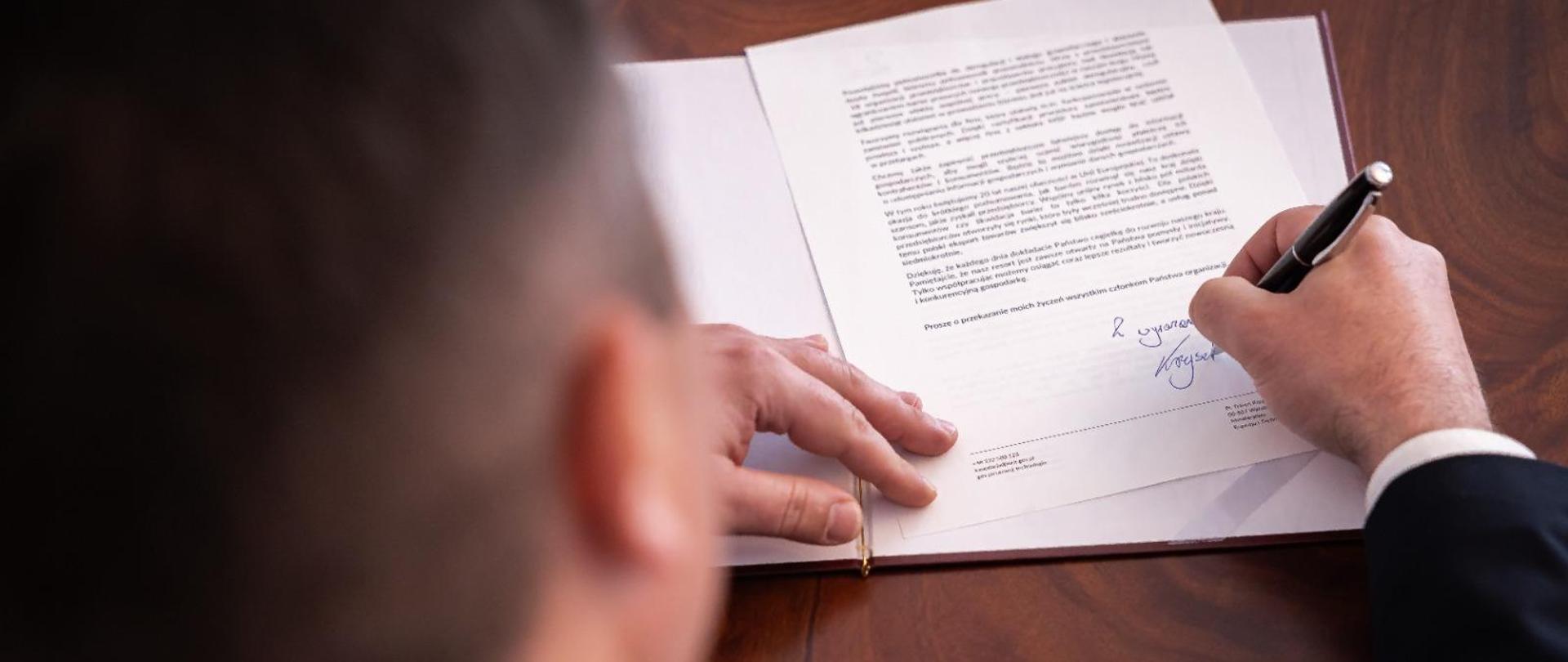Minister Krzysztof Paszyk podpisuje list gratulacyjny do przedsiębiorców