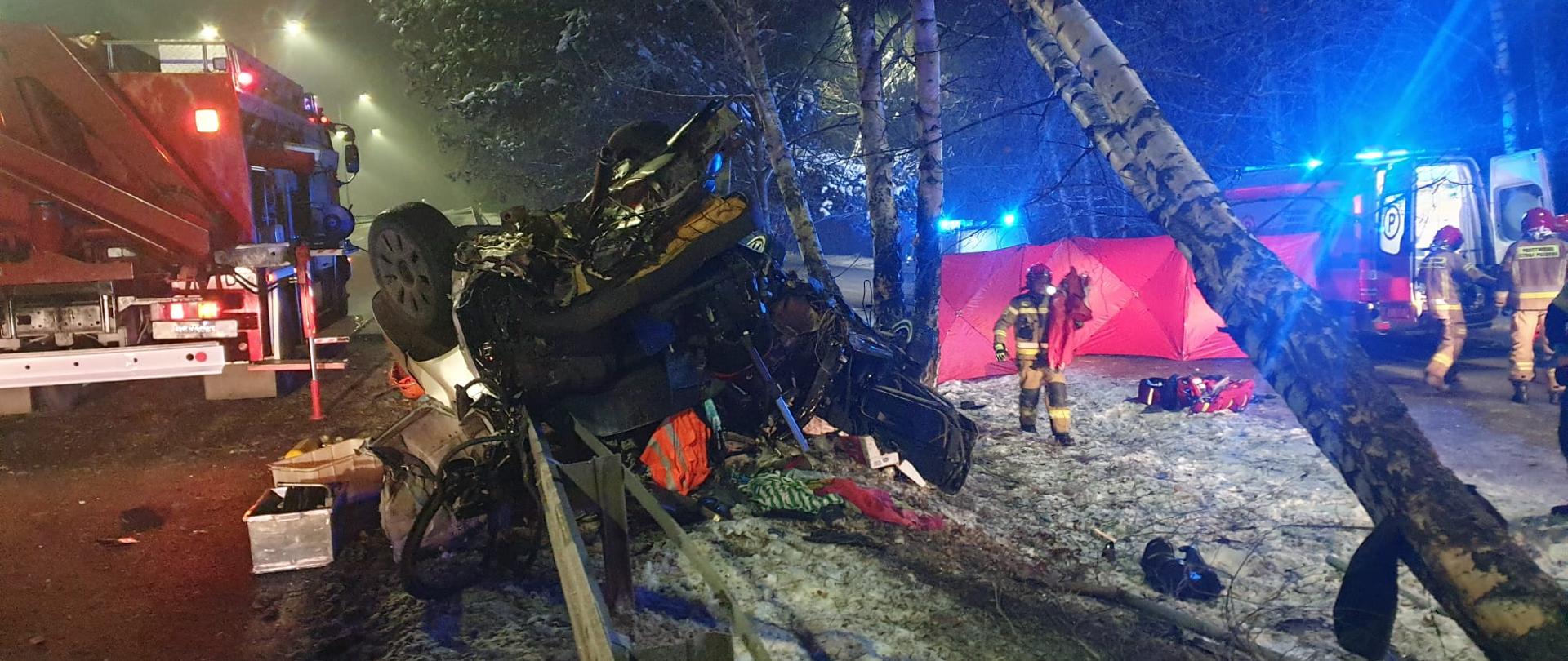 Rozbity samochód oparty na podnośnikach kolumnowych w tle samochód PSP i pogotowia