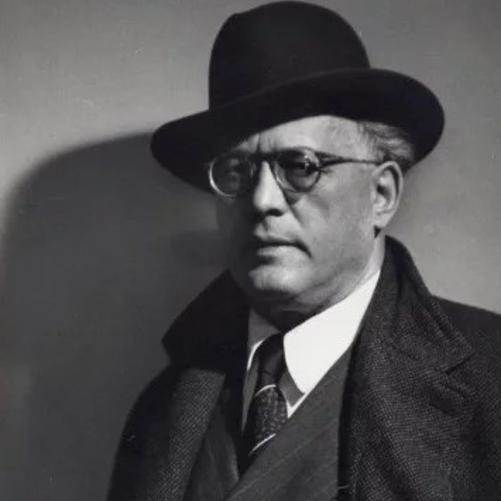 Czarno-białe zdjęcie przedstawiające sylwetkę Grzegorza Fitelberga w garniturze, płaszczu i kapeluszu